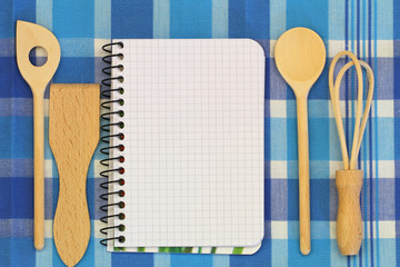 Notebook and wooden cooking utensils on checkered tablecloth