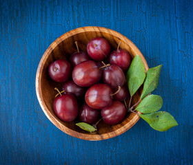 Ripe plums in a wooden bowl on a blue wooden background