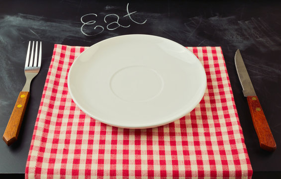 Empty plate with knife and fork on tablecloth over chalkboard