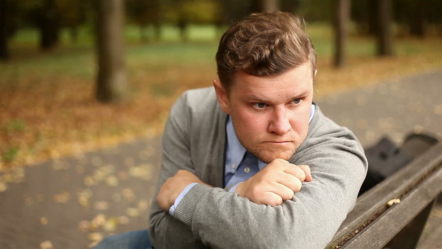 Depressed, sad young businessman sitting in the park, 1080p