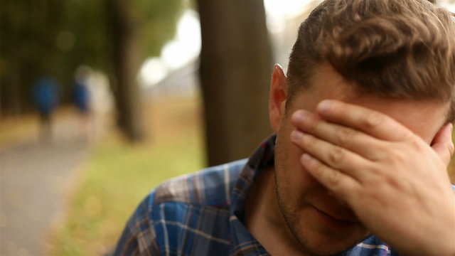 Depressed, sad young man sitting in the park, 1080p