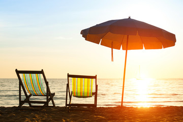 Pair of beach loungers on deserted coast sea at sunrise