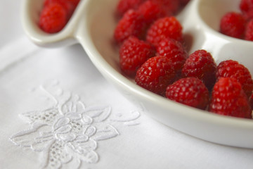 Closeup of red raspberries in white bowl on white linen napkin