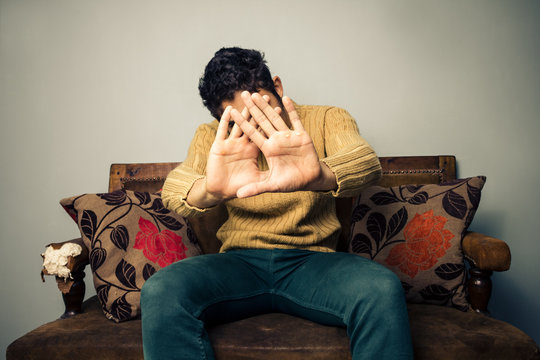 Young man on sofa covering his face