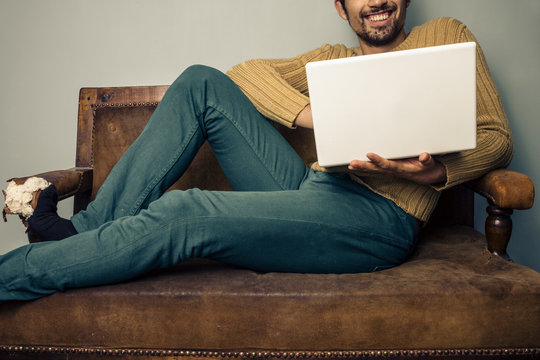 Smiling young man with laptop on old sofa