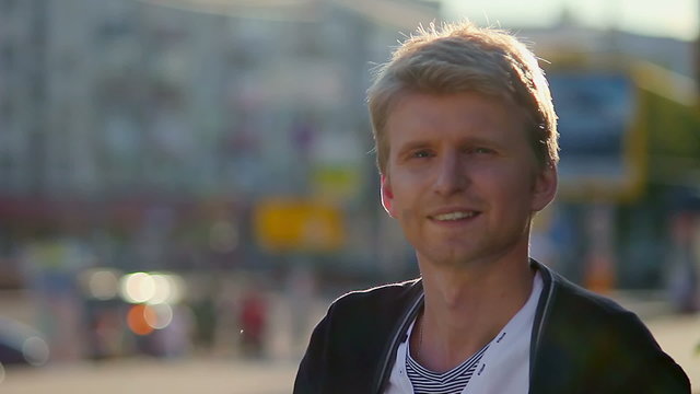 Smiling young man takes off glasses looking at camera city