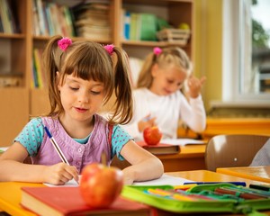 Little schoolgirl sitting behind school desk