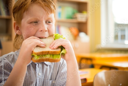 Little redhead schoolboy eating sandwich in class