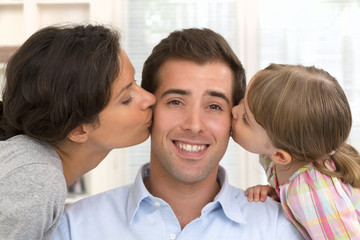 Happy family, mother and daughter kissing father at home