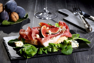 fichi e prosciutto su pietra nera  sfondo grigio 