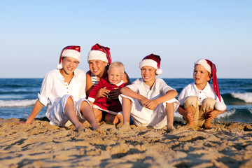 Children in santa claus hat are sitting on beach