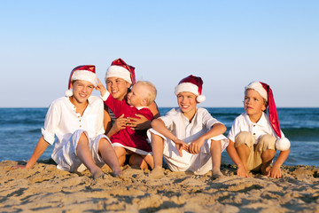 Children in santa claus hat are sitting on beach