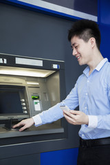 Naklejka na ściany i meble Smiling young businessman withdrawing money from the ATM