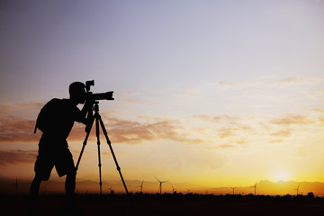 Silhouette of man taking photos with his camera at sunset with a dramatic sky