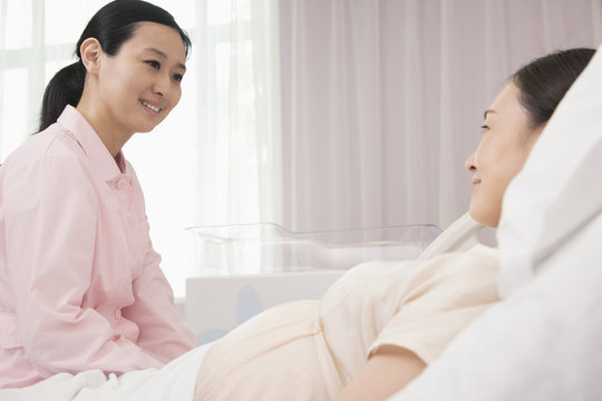 Smiling nurse talking to pregnant woman lying on bed in the hospital