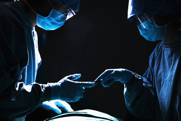 Two surgeons working and passing surgical equipment in the operating room, dark 