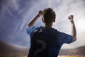 Soccer player with arms raised cheering, stadium with sky and clouds