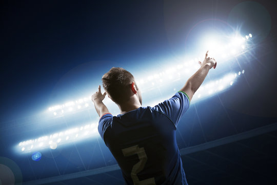 Soccer player with arms raised cheering, stadium at night time