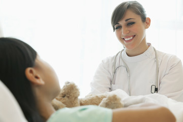 Smiling female doctor talking to girl patient lying down on a hospital bed