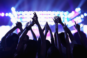 Audience watching a rock show, hands in the air, rear view, stage lights