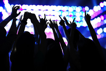 Audience watching a rock show, hands in the air, rear view, stage lights