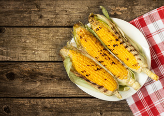 Grilled corn cobs on plate - vintage wood background