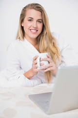 Happy pretty model holding coffee lying on cosy bed