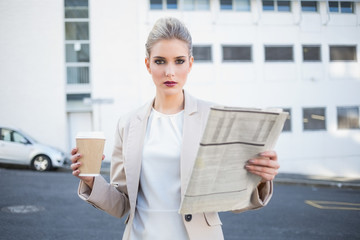 Serious stylish businesswoman holding newspaper and coffee