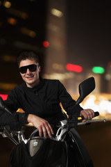 Fototapeta na wymiar Young smiling man in sunglasses sitting on his motorcycle at night in Beijing