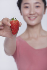 Obraz premium Young smiling woman in pink shirt holding and showing a strawberry 