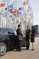 Three businesspeople meeting outdoors with flagpoles in background