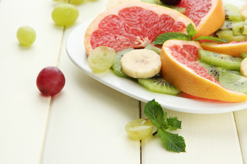 Assortment of sliced fruits on plate, on white wooden table