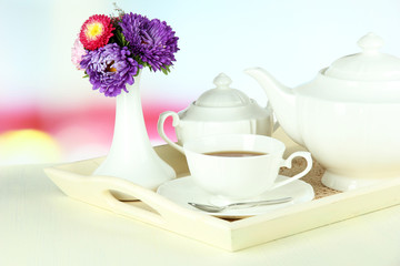 Cup of tea with cakes on wooden tray on table in room