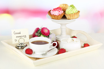 Cup of tea with cakes on wooden tray on table in room