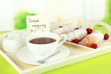 Cup of tea with cakes on wooden tray on table in room