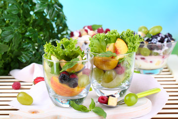Fruit salad in glasses, on wooden table, on bright background