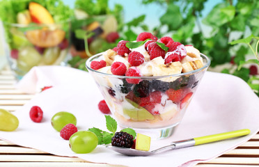 Fruit salad in bowl, on wooden table, on bright background
