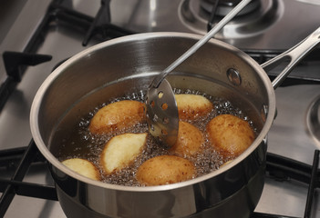 Doughnuts frying in a boiled oil stirring by skimmer