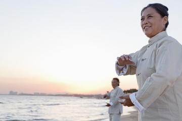 Two older people practicing Taijiquan on the beach at sunset, China
