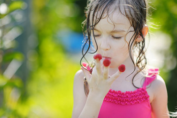 Adorable little girl eating raspberries