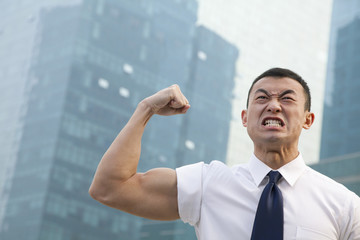 Portrait of young angry businessman flexing muscles