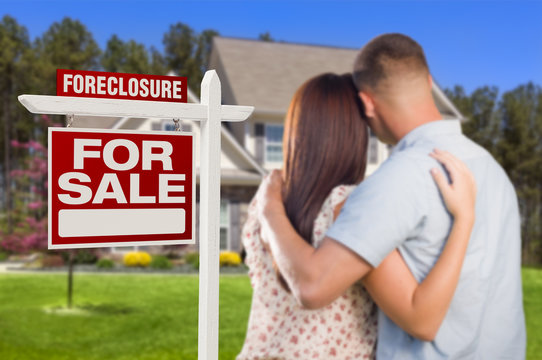 Military Couple Standing In Front Of Foreclosure Sign And House