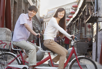 Fototapeta premium Side View of Young Heterosexual Couple on a Tandem Bicycle in Beijing Looking at Camera