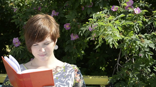Pregnant woman reading notebook on the bench and smiling