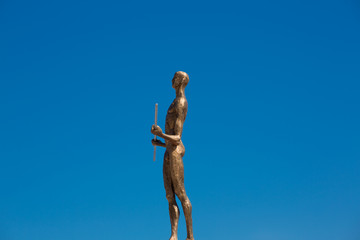 Statue made of bronze of a naked man with blue sky in the backgr