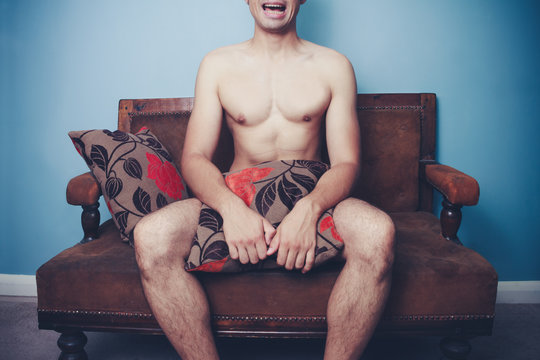 Young naked man on sofa with disturbed look on his face