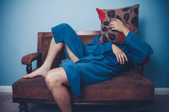 Man in dressing gown hiding behind cushion