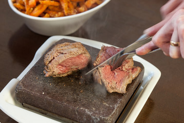 Steak sizzling on hot stone plate being sliced