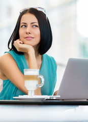 Girl  sits at the table of the bar and works at the pc