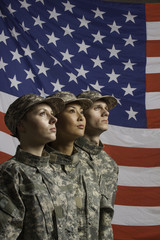 Three young military personnel in front of flag, vertical